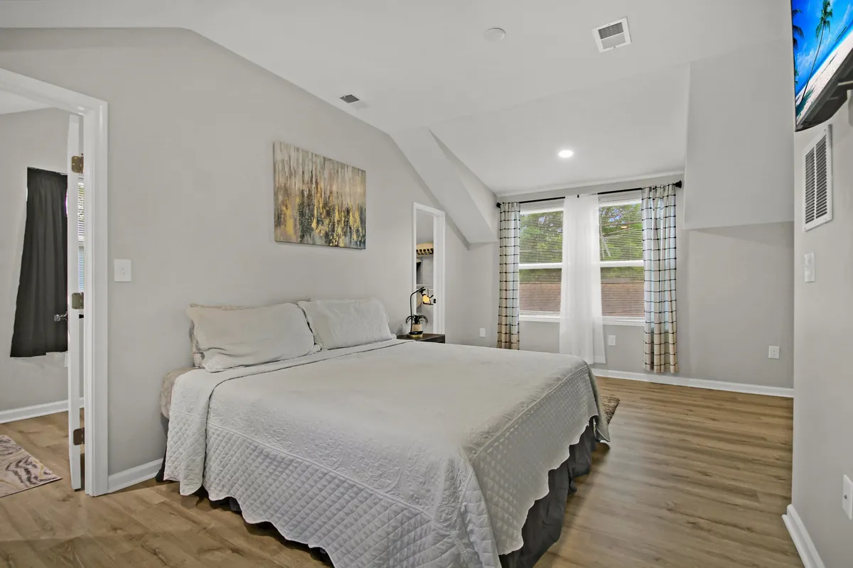 A serene bedroom featuring a neatly made bed with comfortable linens, window with elegant curtains, calming artwork above the headboard, and soft lighting. The arrangement highlights restful sleep and a private, tranquil atmosphere.