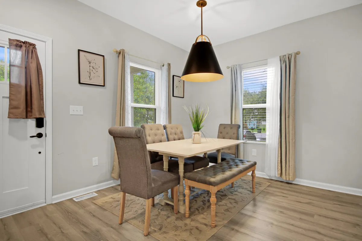 A cozy dining area featuring a dining table set beneath a stylish hanging light fixture, with ample natural light streaming through the windows. The setup invites intimate meals and heartfelt conversations.