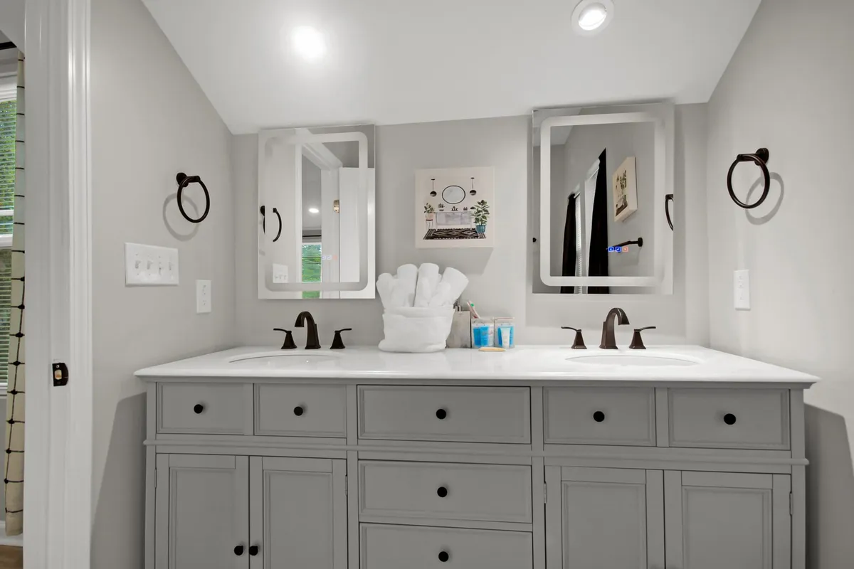 A bright, modern bathroom featuring a double sink vanity with stylish mirrors, soft lighting, and decorative art. The setup exudes a spa-like, calming atmosphere ideal for personal routines and relaxation.