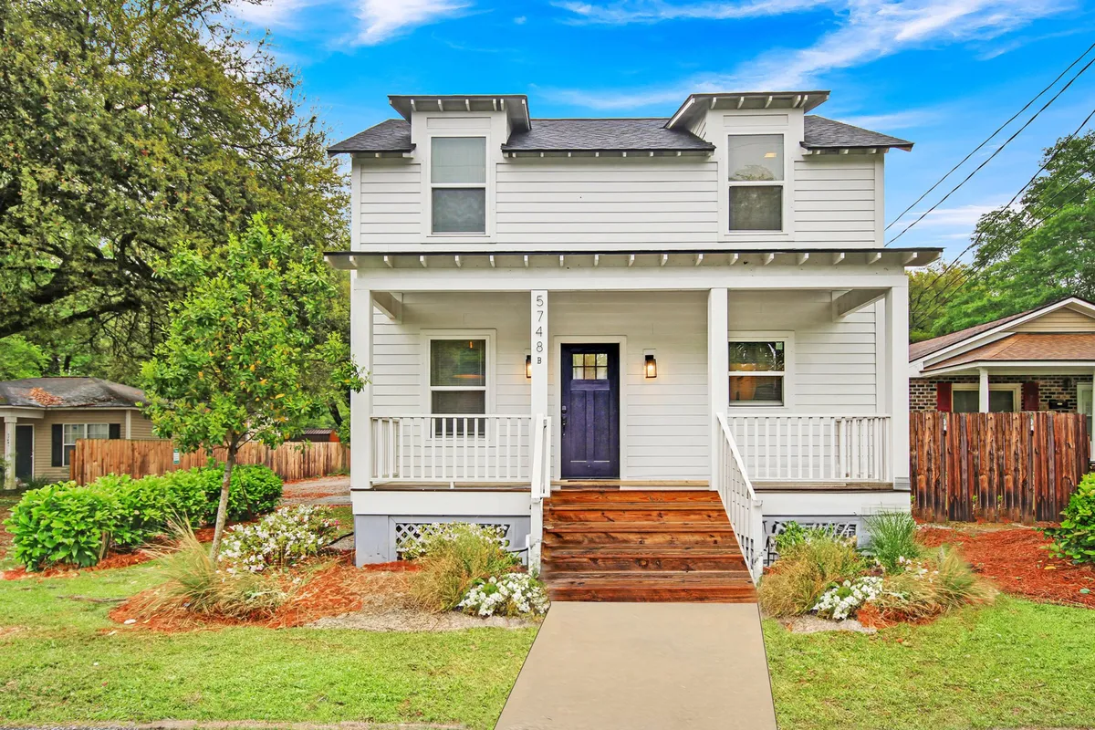 A cheerful view of the home's front porch with a distinctive purple door, manicured landscaping, and inviting steps leading up from the yard. The scene exudes a sense of welcome and comfort, suggesting easy access for travelers arriving after a journey.