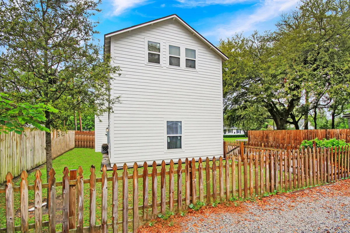 A welcoming two-story modern home features a lush green lawn, wooden fence, and a backdrop of mature trees, blending suburban comfort with inviting curb appeal.